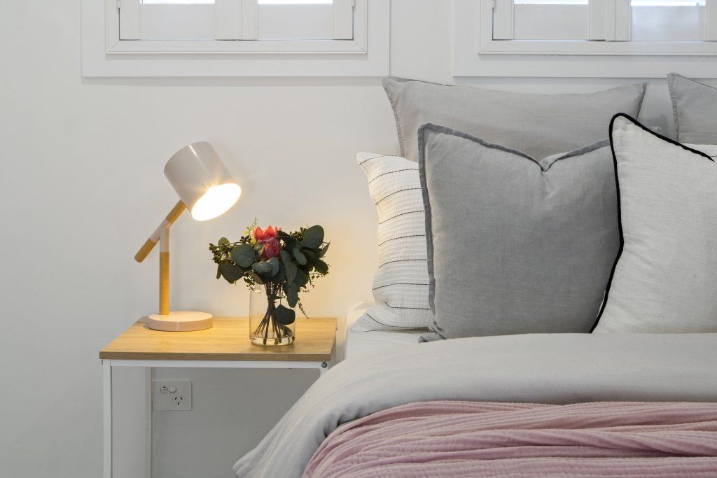 A bed with a lamp and a vase of flowers on a nightstand.