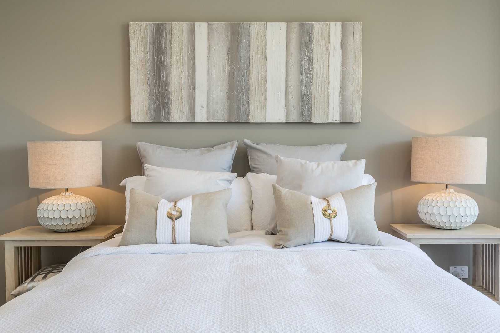 A bedroom with a bed , two lamps and a painting on the wall above the bed.