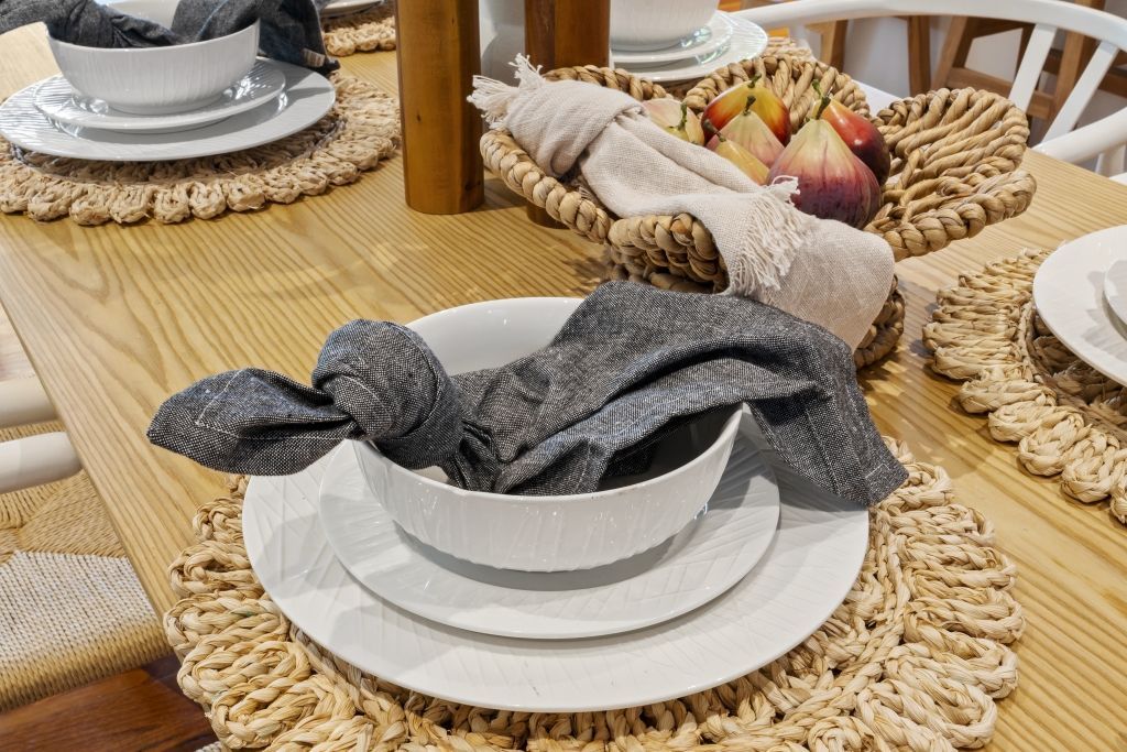 A dining room table with plates , bowls , and napkins on it.