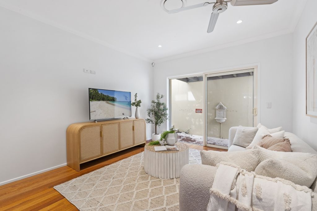 A living room with a couch , table , television and ceiling fan.
