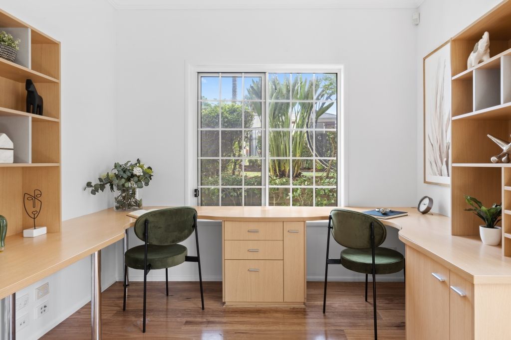 A room with two desks and two chairs in front of a window.