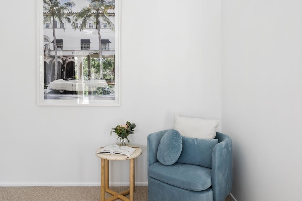 A living room with a blue chair , a table , and a picture on the wall.