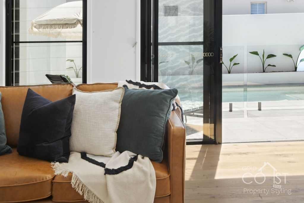 A living room with a couch and pillows and a pool in the background.