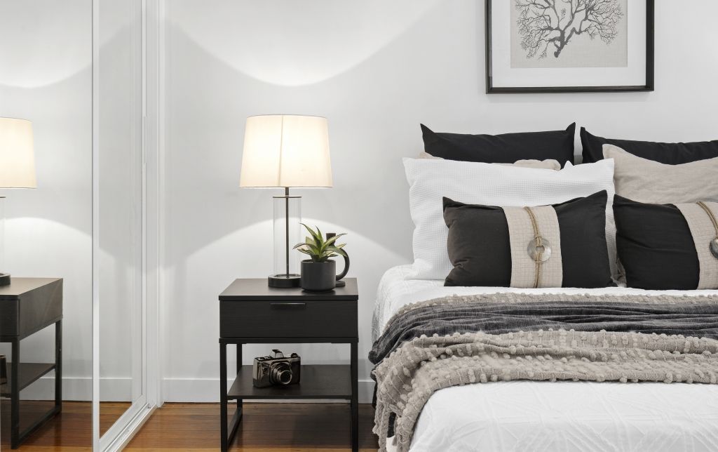 A bedroom with a bed , nightstand , lamp and mirror.