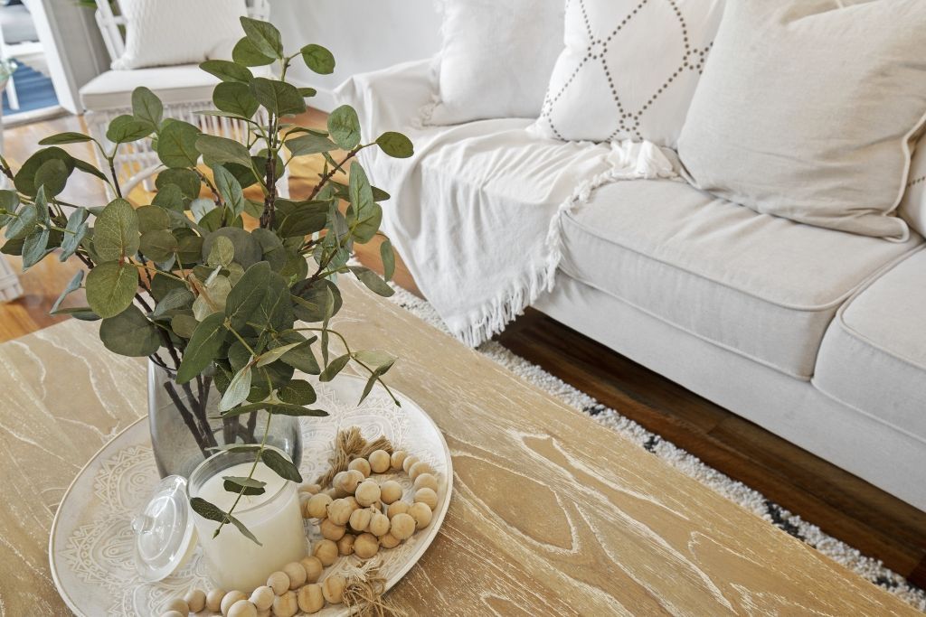 A living room with a white couch and a table with a vase of flowers on it.