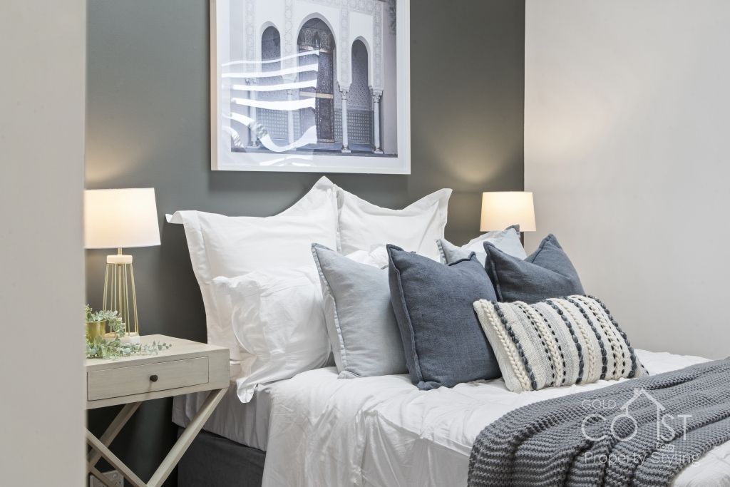 A bedroom with a bed , nightstand , lamps and a picture on the wall above the bed.