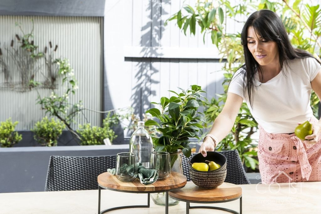 A woman is standing at a table with a bowl of lemons on it.