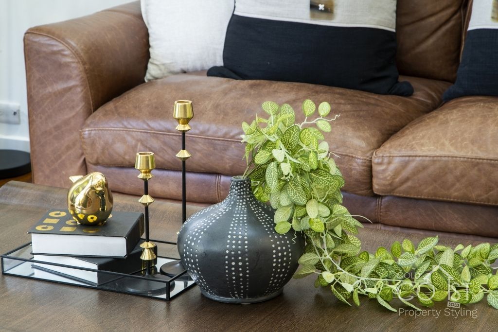 A living room with a brown leather couch and a black vase with a plant in it.