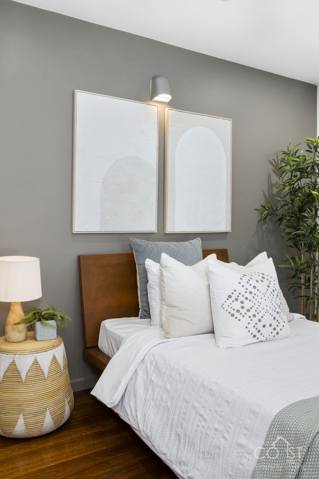 A bedroom with a bed , nightstand , lamp and paintings on the wall.