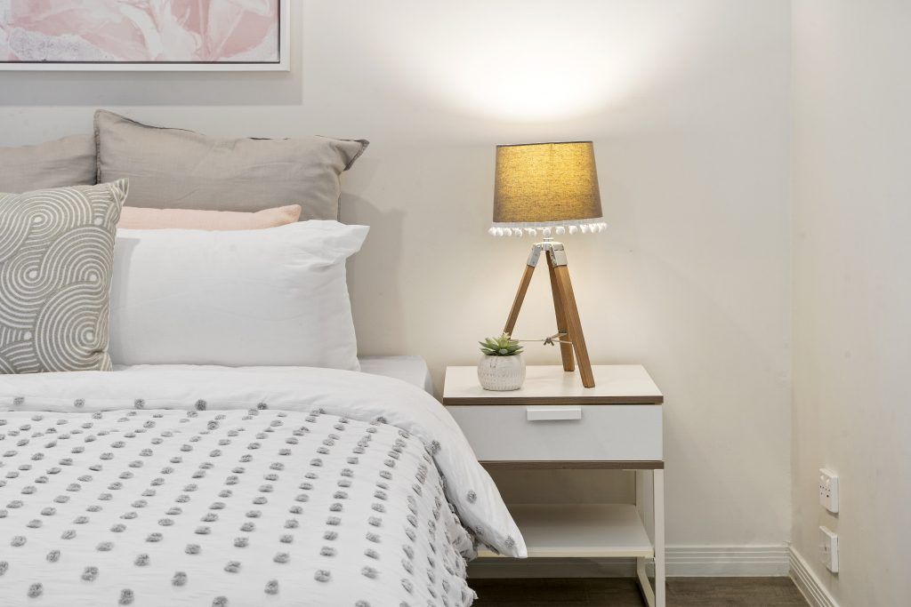 A bedroom with a bed , nightstand , lamp and picture on the wall.