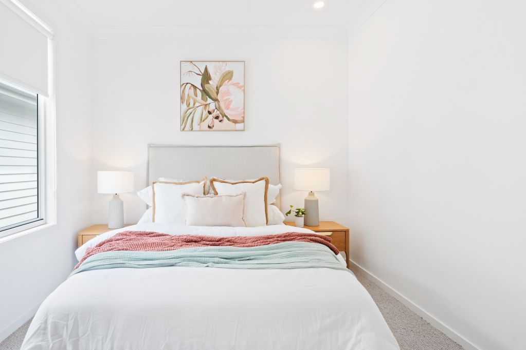 Bright minimalist bedroom with a white bed, colorful throw blanket, and framed wall art