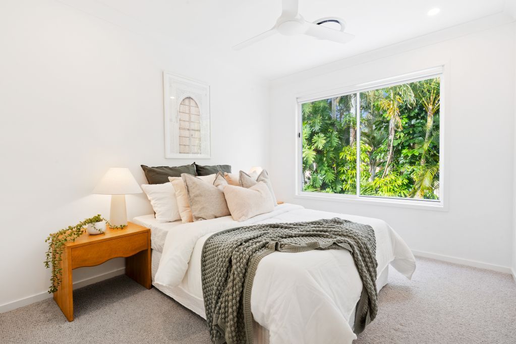 Bright bedroom with a bed, wooden nightstand, and a large window looking onto greenery