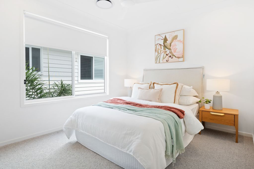Bright modern bedroom with white bedding, wood nightstand, large window, and wall art