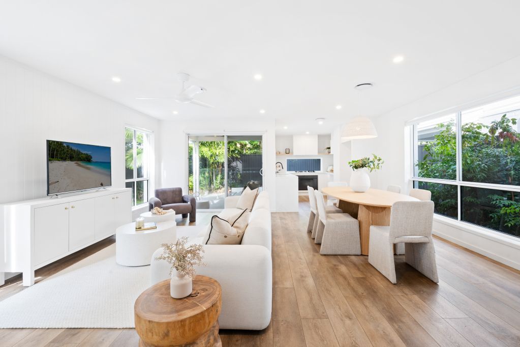 Bright open-plan living room and dining area with white furniture, wood floors, and large windows