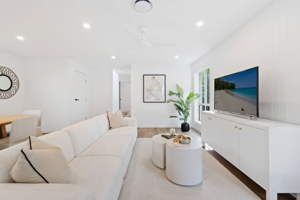 Bright modern living room with a white sofa, round tables, plant, and TV on a low console.