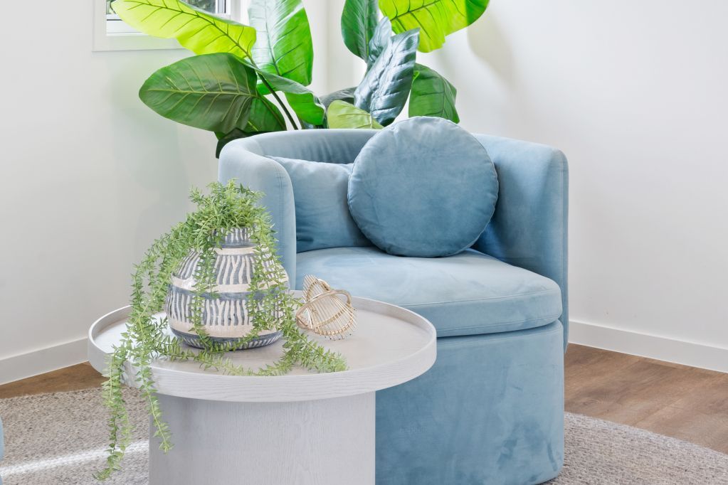 Light blue armchair with round pillow beside a white table and green plants in a bright room