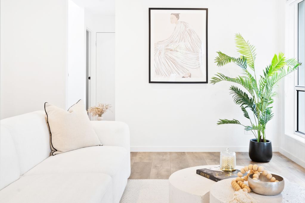 Bright minimalist living room with white sofa, framed art, coffee table, and tall potted plant