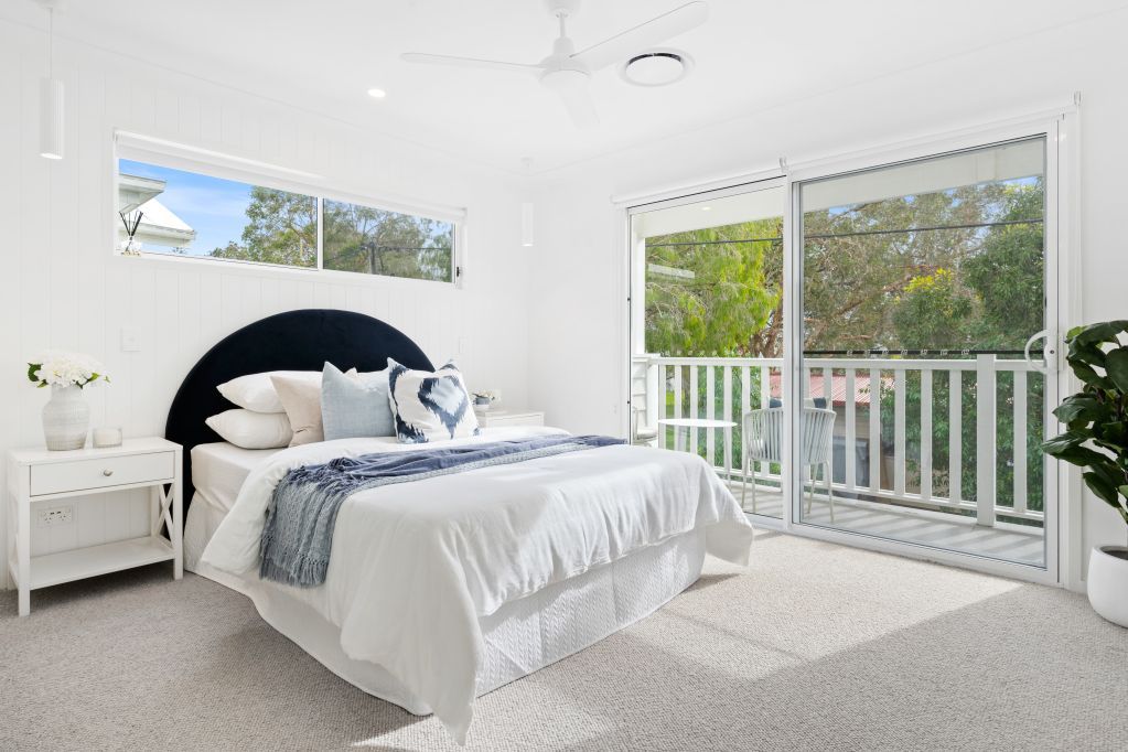 Bright white bedroom with a bed, nightstand, and large windows opening to a balcony and green view