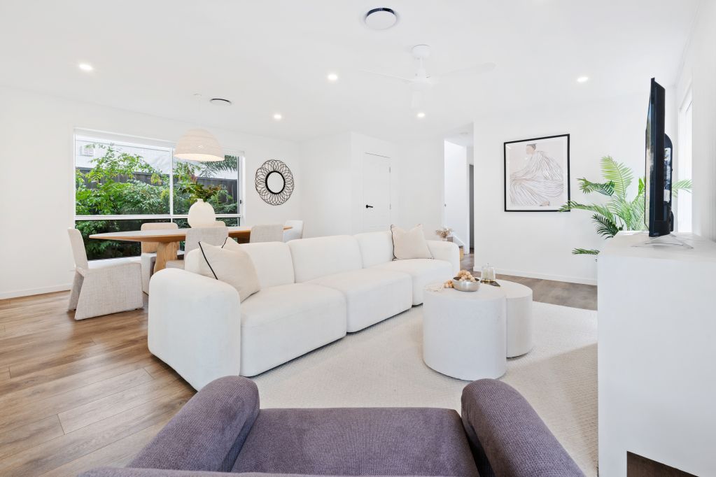 Bright modern living room with white sofas, wood floors, large windows, and minimalist decor