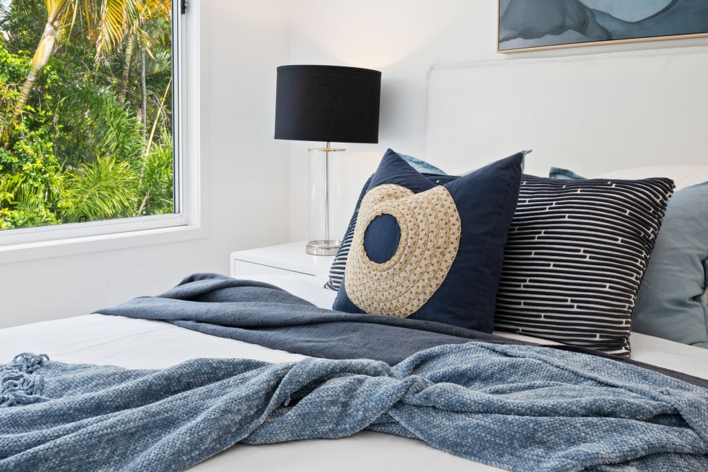 Neatly made bed with blue bedding, patterned pillows, and a black lamp beside a bright window