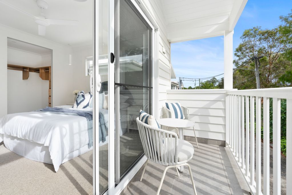 Bright bedroom opening to a white balcony with chairs and sunlight