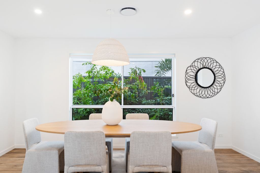 Bright dining room with round wooden table, beige chairs, large window, and decorative wall mirror