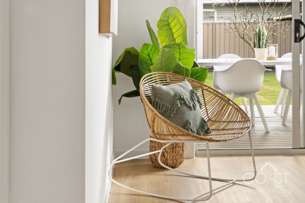 A wicker chair with a pillow on it is in a living room next to a potted plant.