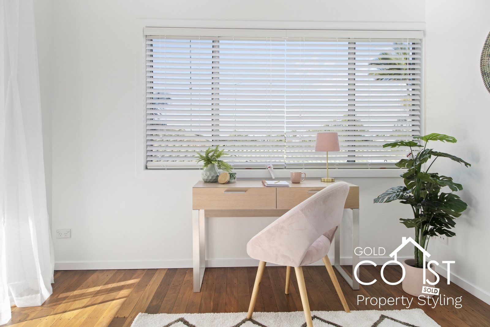 A room with a desk and chair in front of a window with blinds.