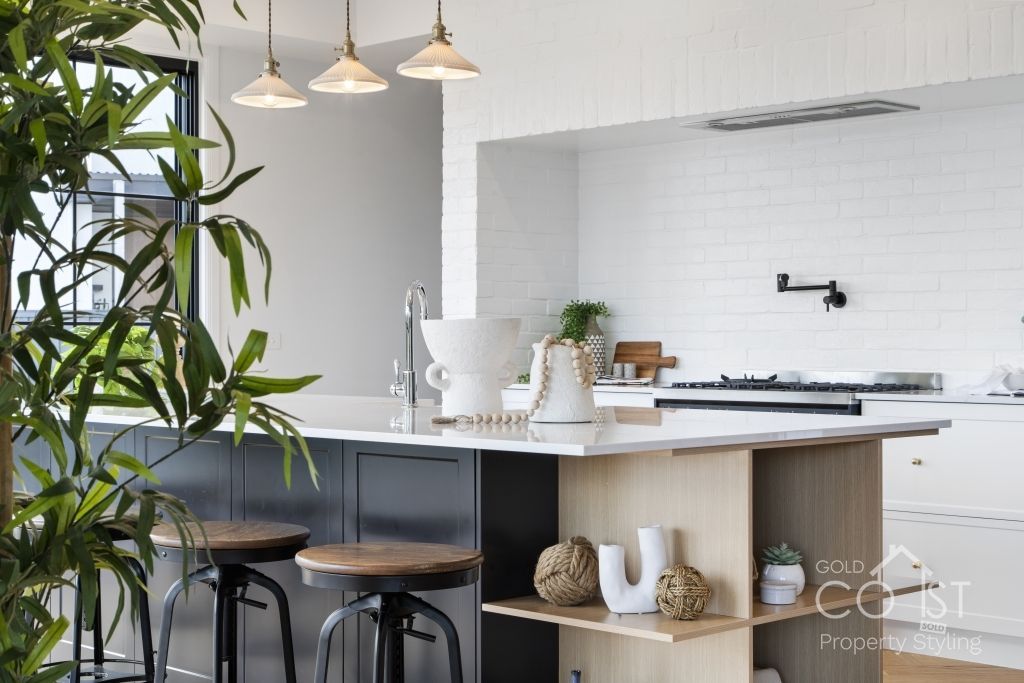 A kitchen with a large island and stools and a plant in the background.