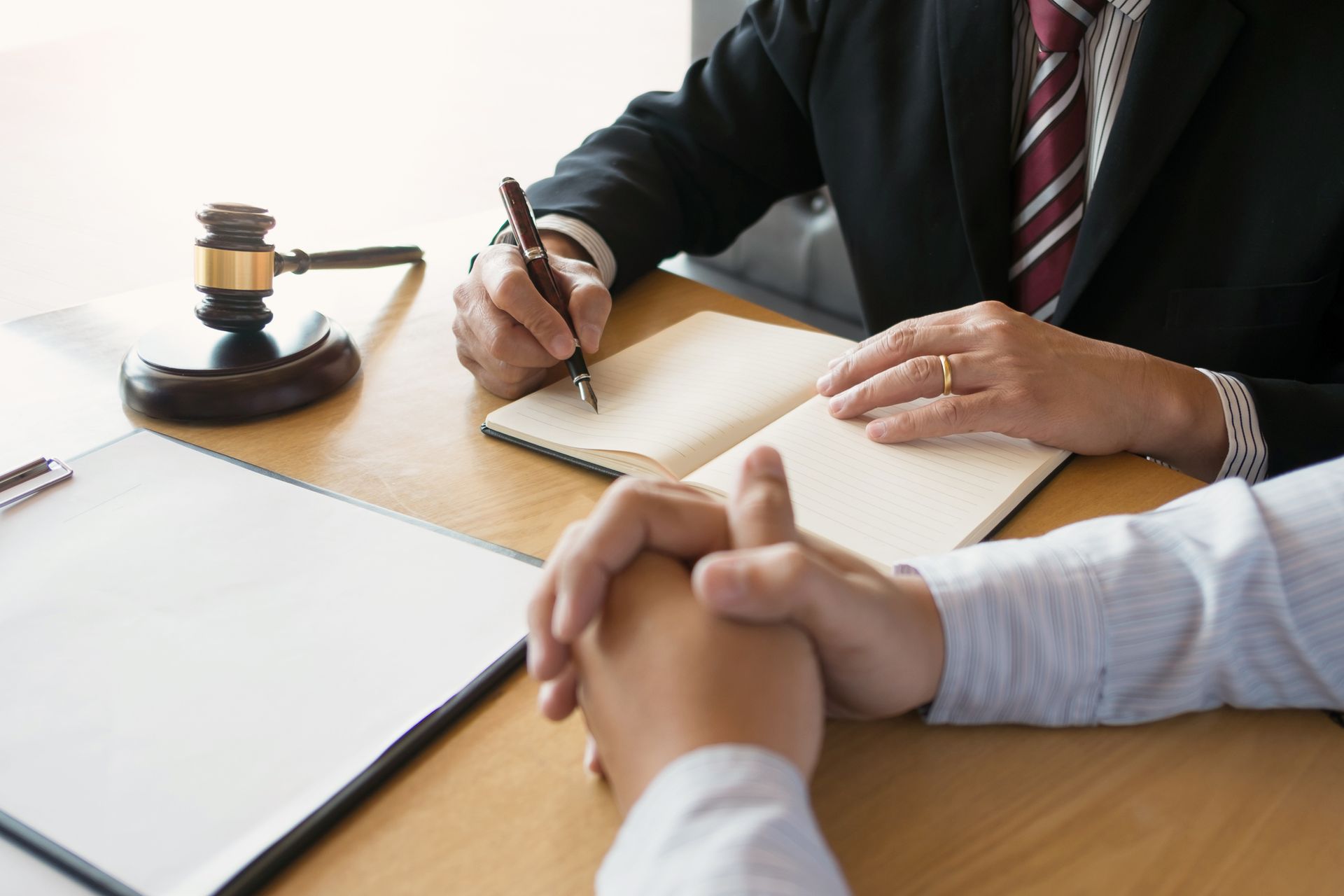 Lawyer in suit writing while meeting with client; gavel on desk.