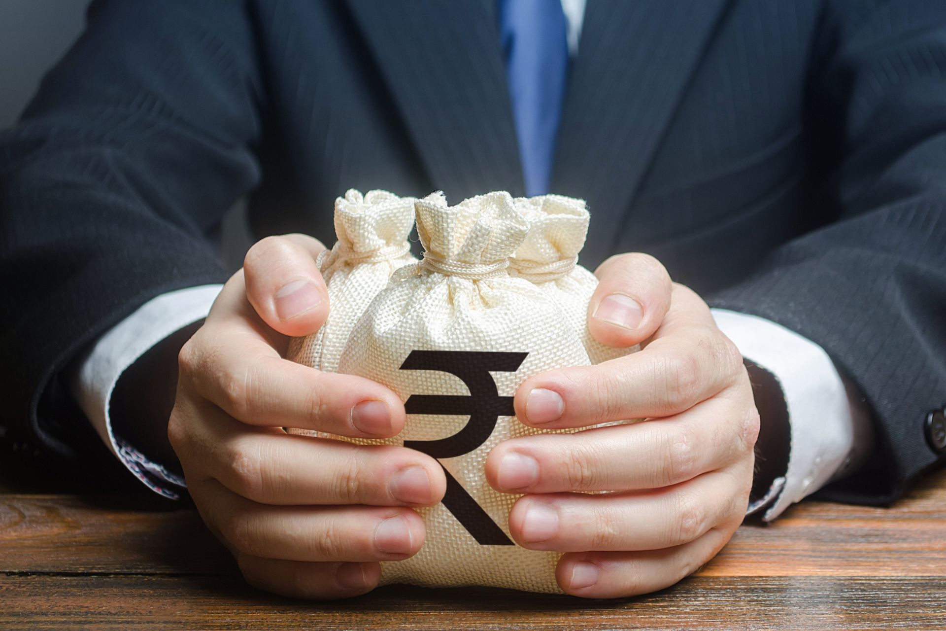 Man in suit holding two money bags with Indian rupee symbol.