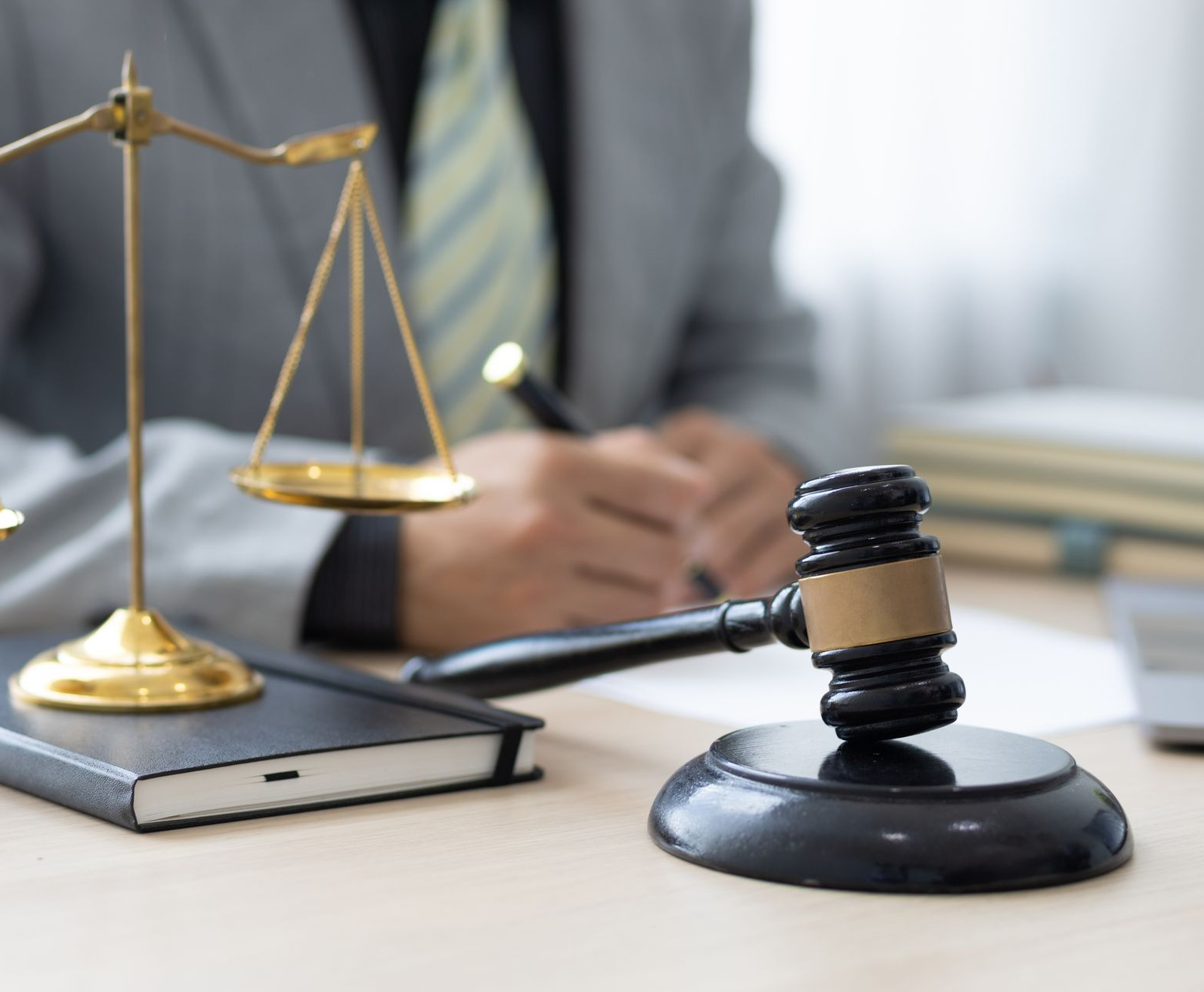 Gavel and scales of justice on desk, a person writing in background. Legal setting.