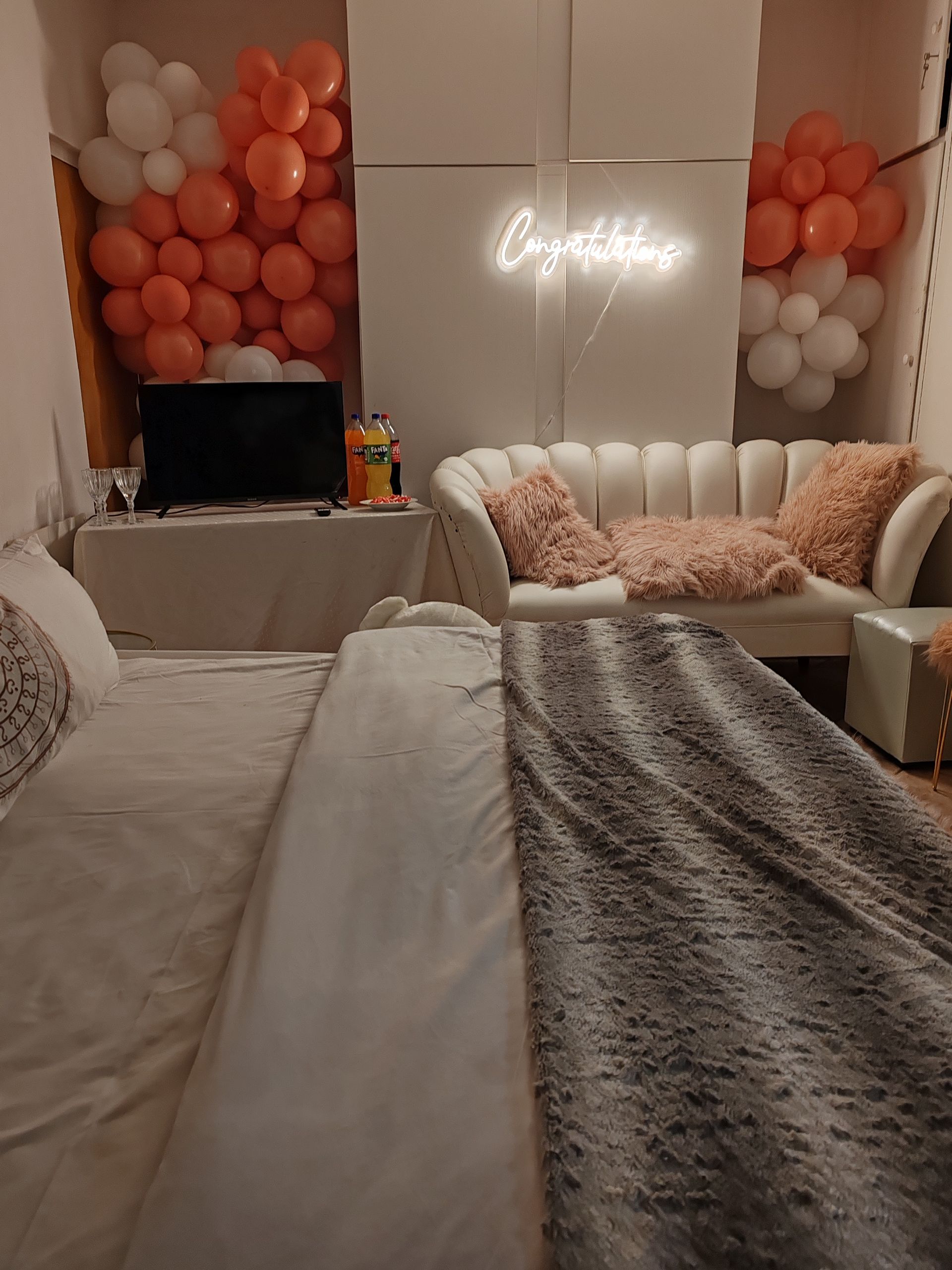 Cozy living room with pink-and-white balloon decor, neon wall sign, couch, and draped blankets