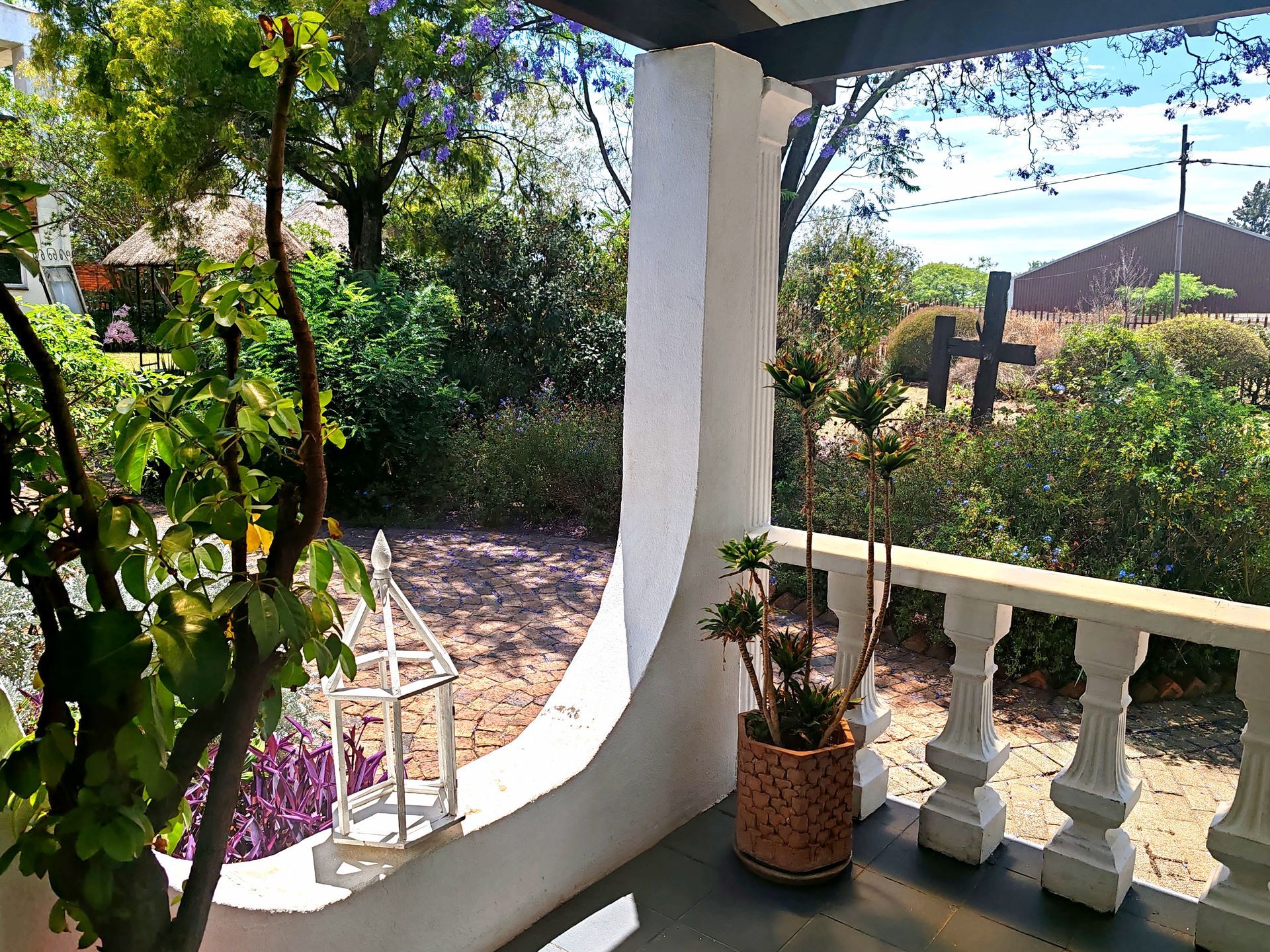 Sunny porch with white railing, potted plants, and a garden view beyond the archway
