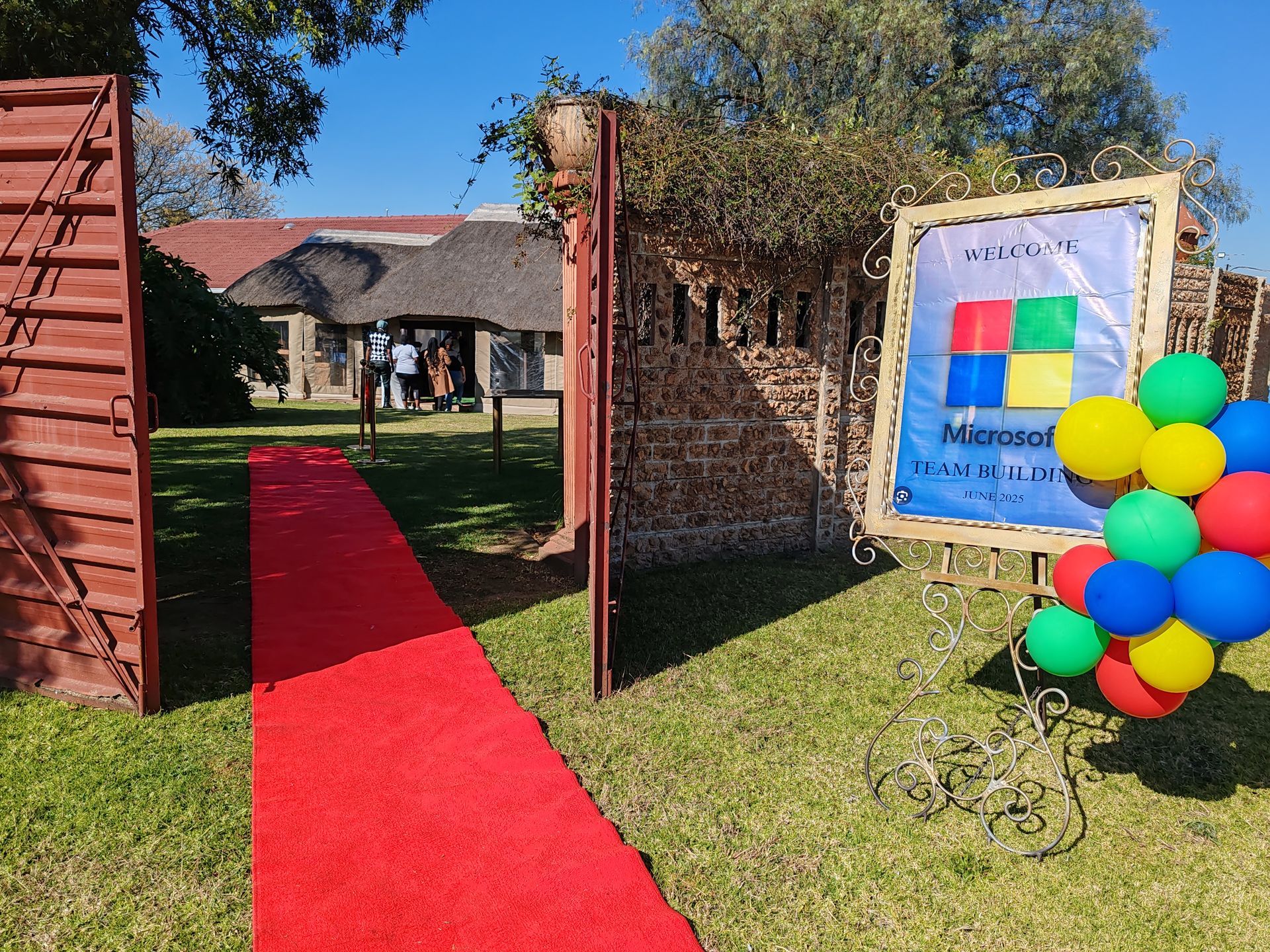 Red carpet entrance with balloons and a framed sign at an outdoor event venue