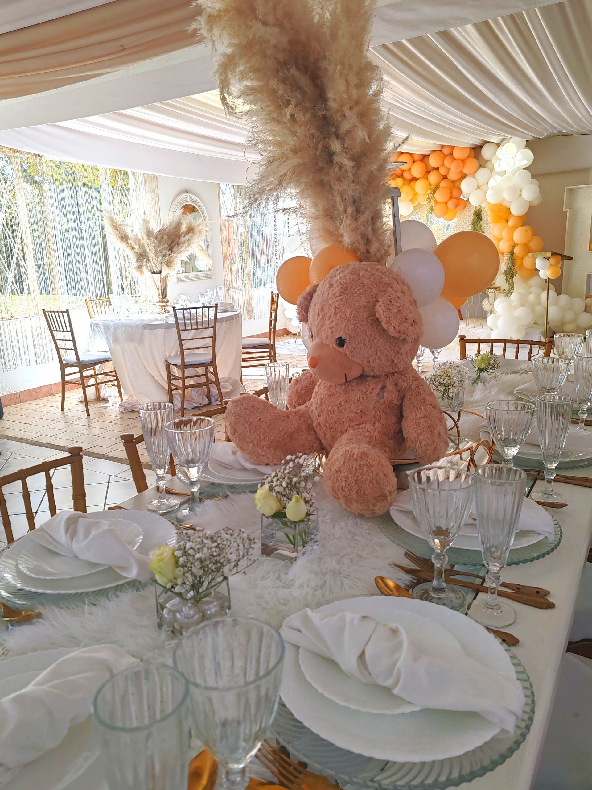 Elegant party table with pink teddy bear centerpiece and white decor under a tent