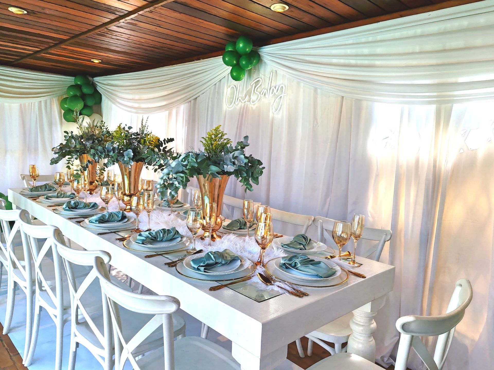 Elegant banquet table with white chairs, floral centerpiece, and green balloons under draped white tent walls