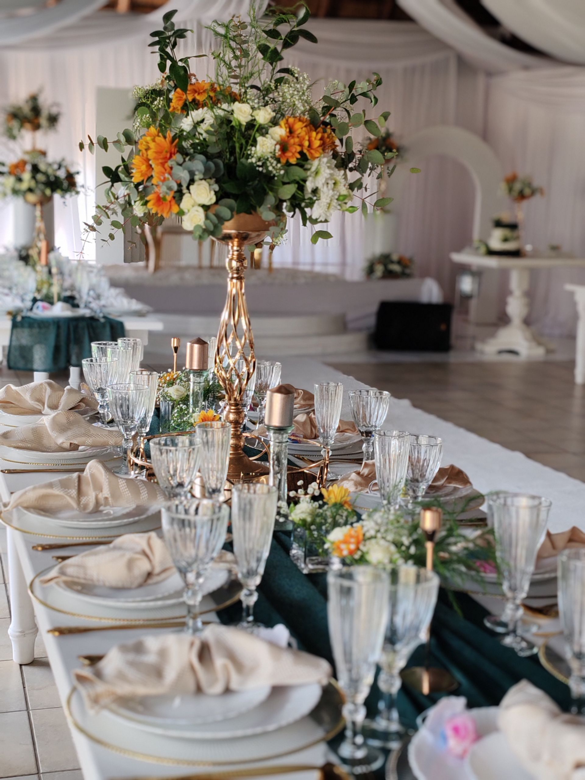 Elegant banquet table with white tableware, teal accents, and orange floral centerpiece in a bright reception hall