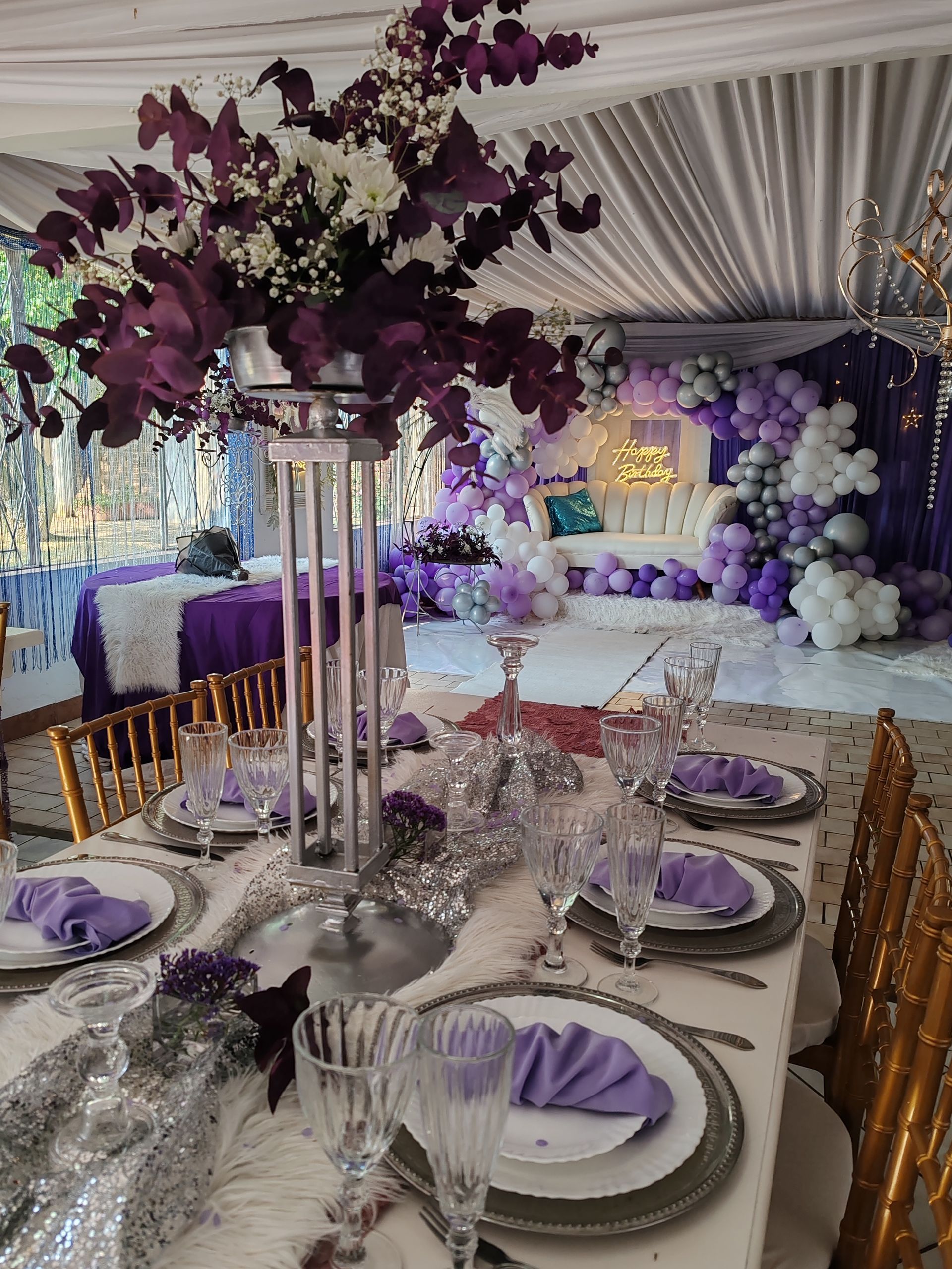 Elegant purple-and-white banquet table with floral centerpiece in a decorated event tent