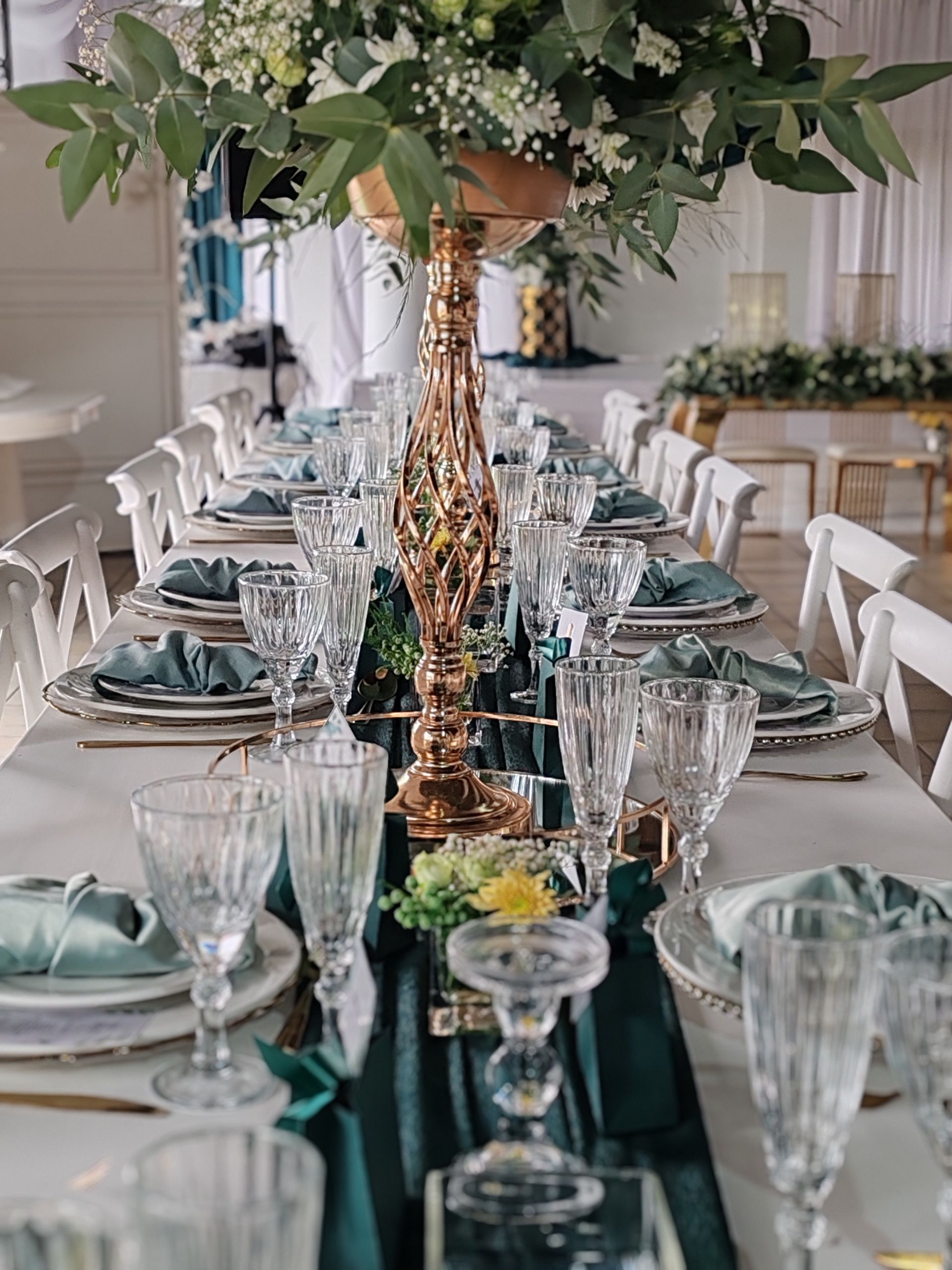 Elegant dining table set for a formal event, with glassware, teal accents, and a leafy centerpiece