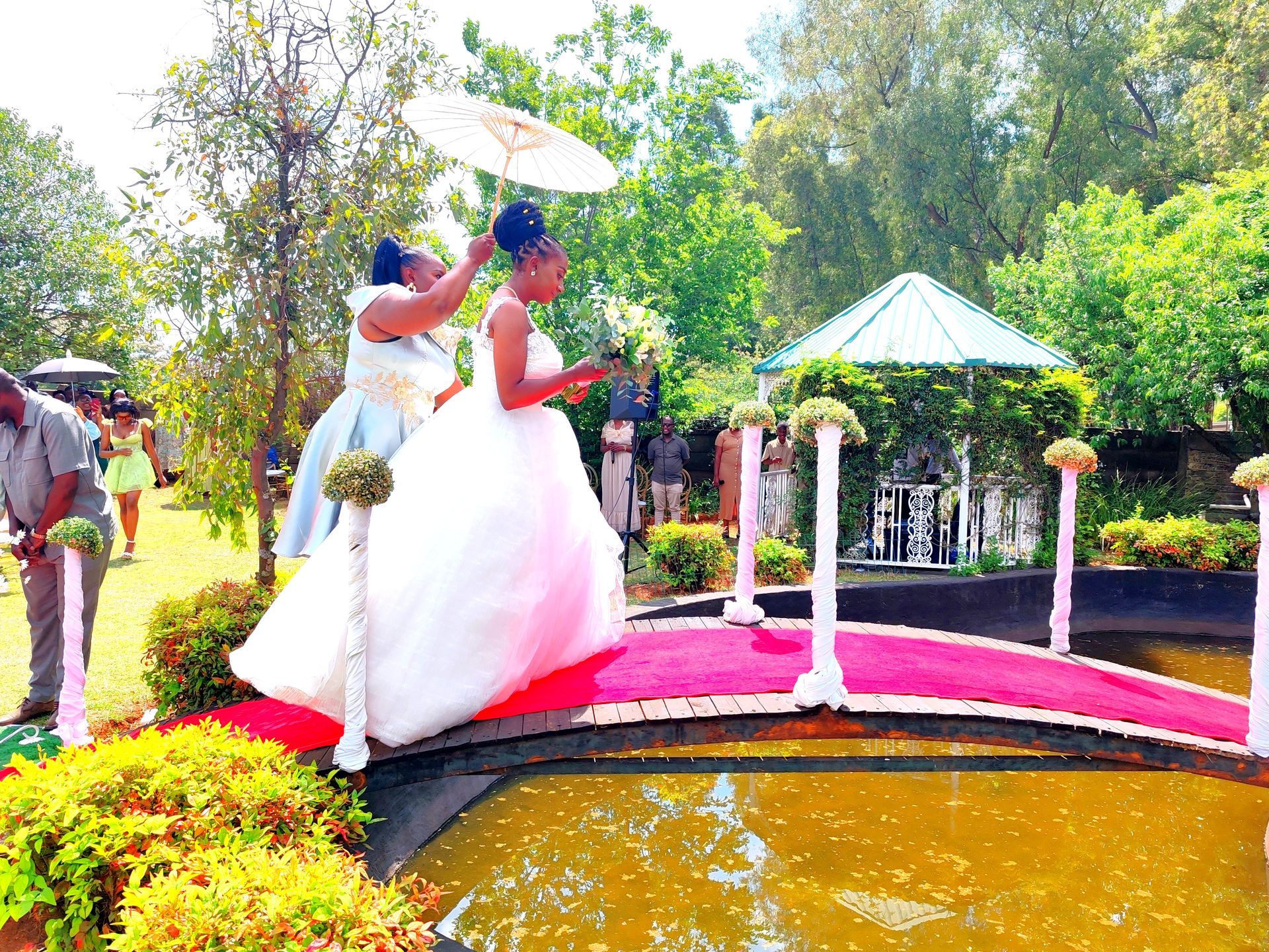 Bride and groom on a pink bridge over a pond in a sunny garden outdoors