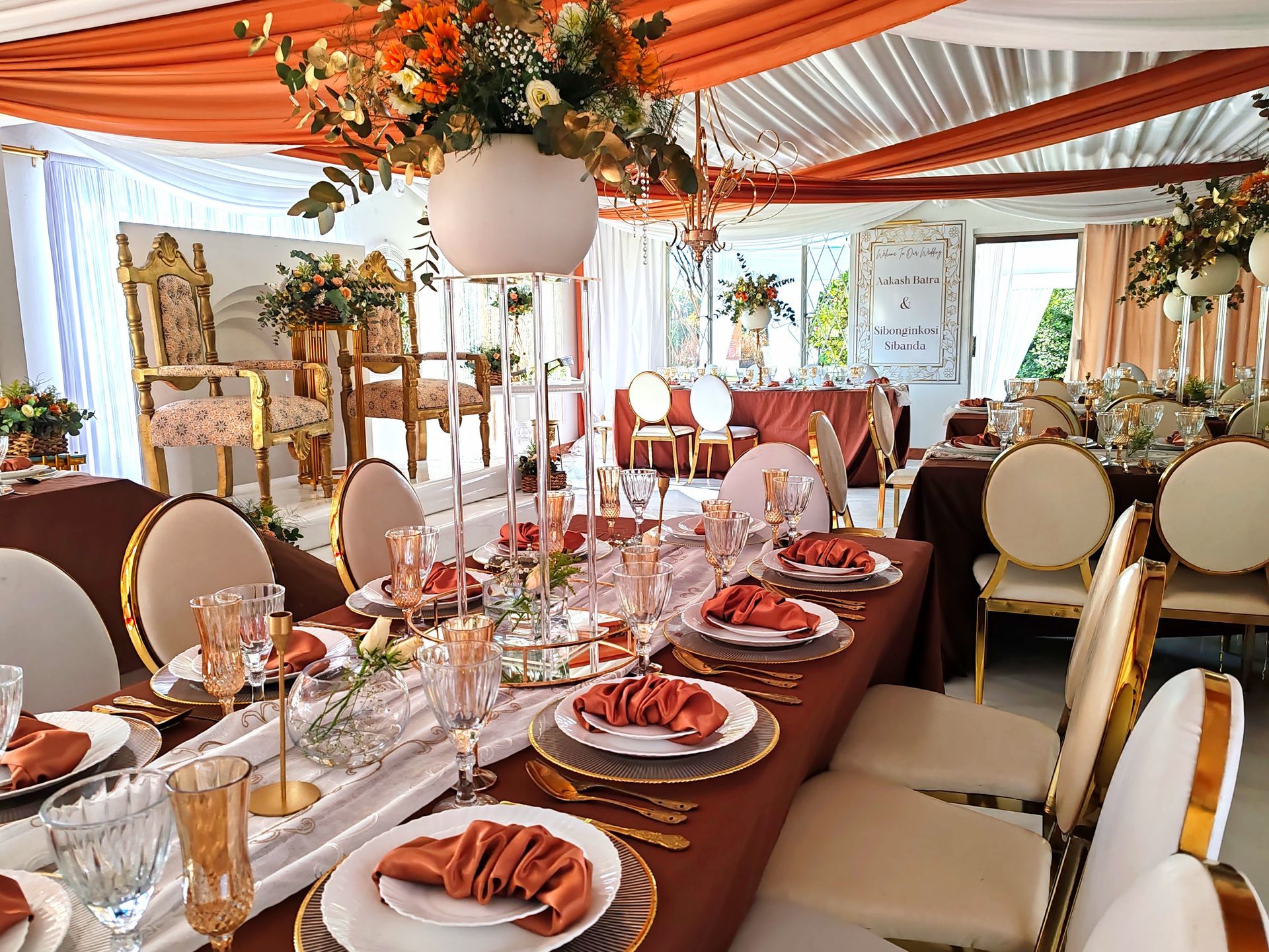 Elegant banquet table under orange drapes with floral centerpiece and gold chairs in a decorated reception hall