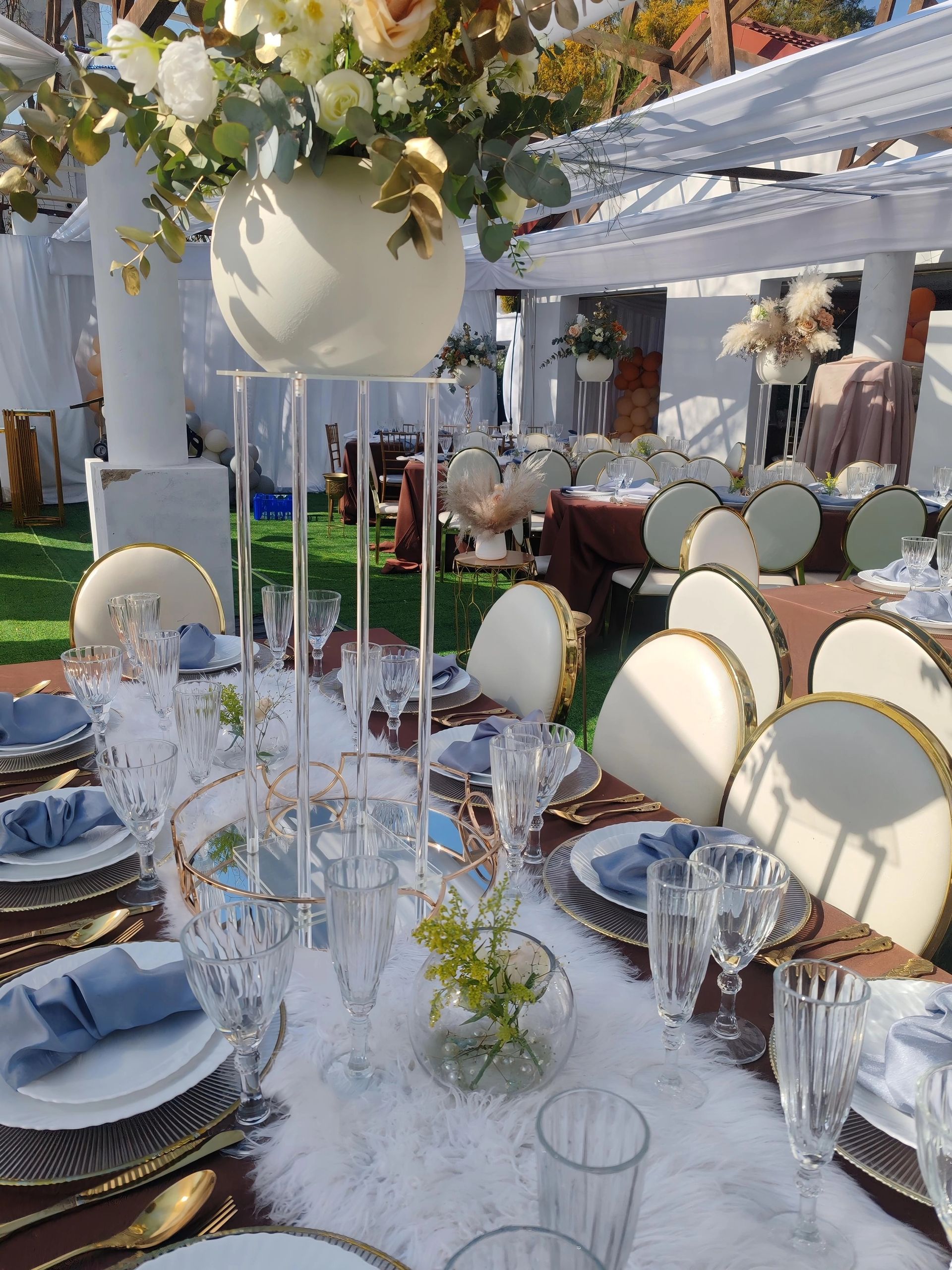 Elegant outdoor banquet table with white floral centerpieces and blue napkins under a canopy