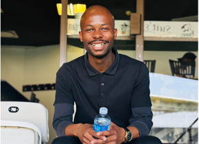Smiling man in a dark polo holding a water bottle while seated indoors