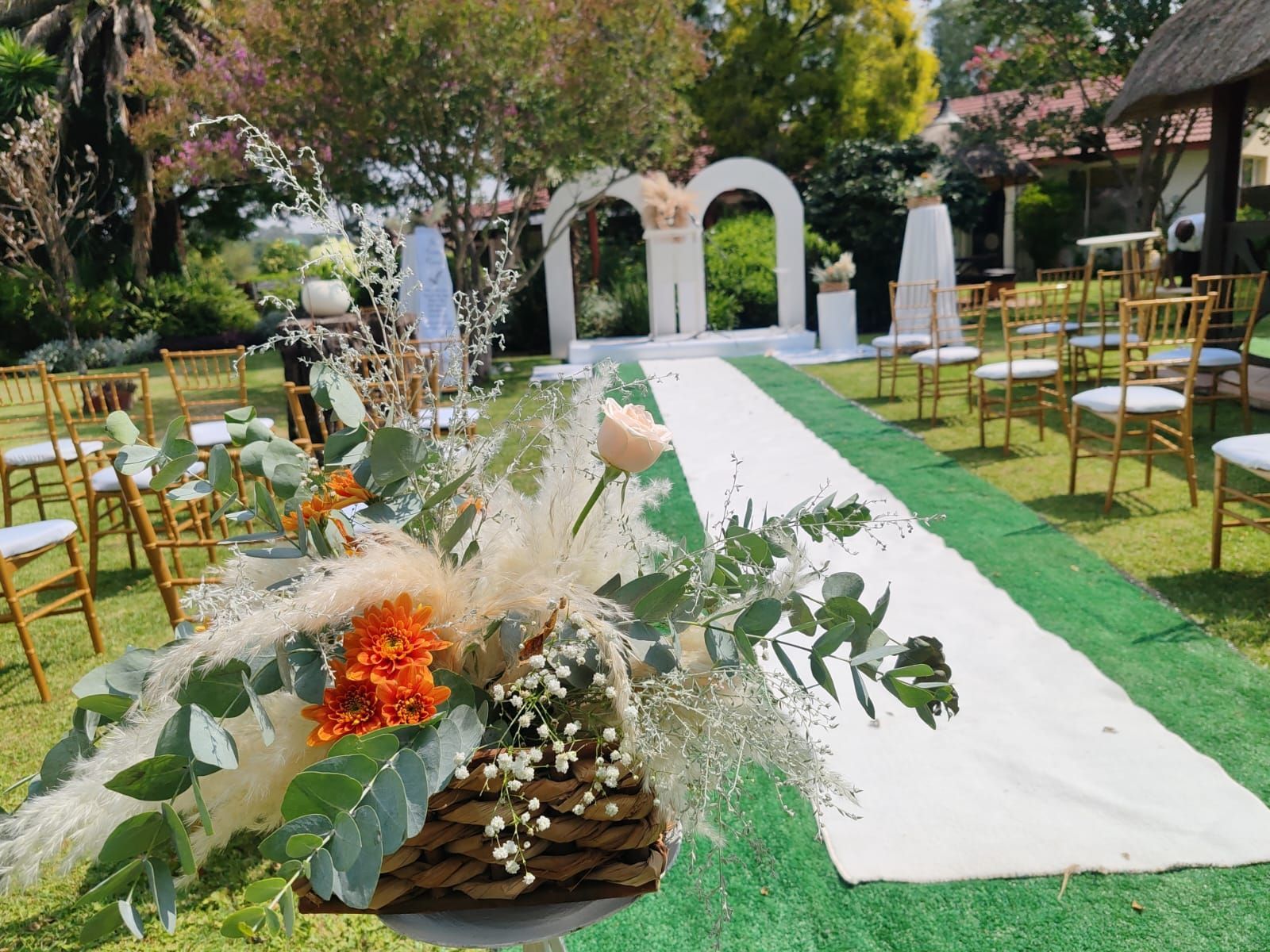 Outdoor wedding aisle with white runners, floral decor, and gold chairs in a garden venue