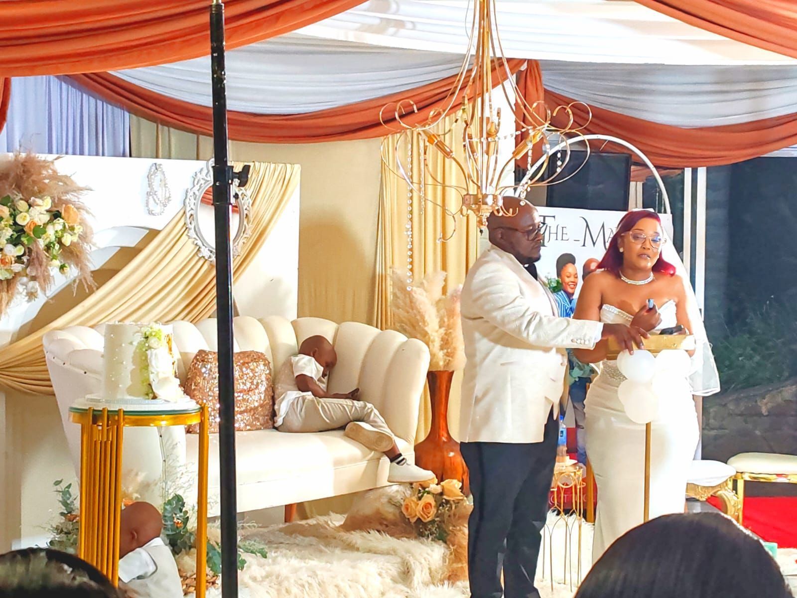 Wedding ceremony under orange and white drapes, with a couple exchanging vows beside a decorated altar.