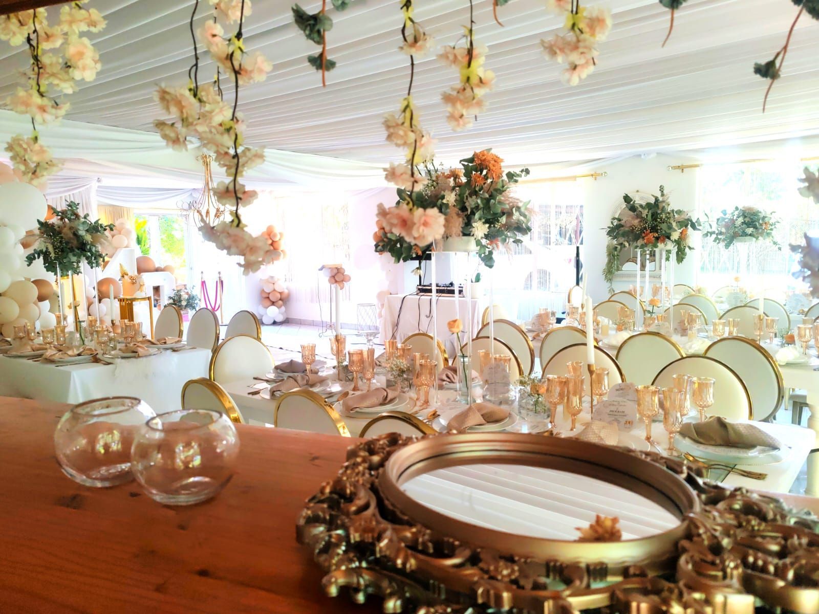 Elegant banquet hall with floral centerpieces, gold accents, and set tables under a white tented ceiling