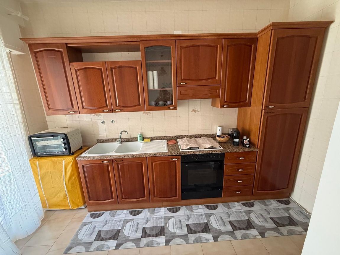 Una cucina con mobili in legno, lavello, piano cottura a gas con forno e lavatrice accanto a una porta luminosa.