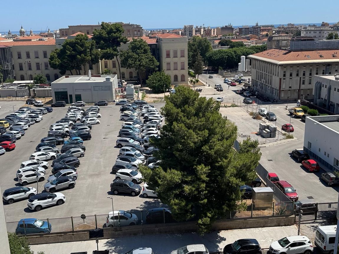 Un divano a fantasia è addossato a una parete bianca, con un tavolino da caffè bianco, un vaso di fiori rossi e una porta sullo sfondo.