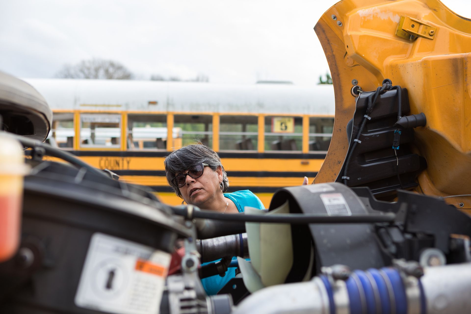 A woman is working on the engine of a school bus. A woman is working on the engine of a school bus.